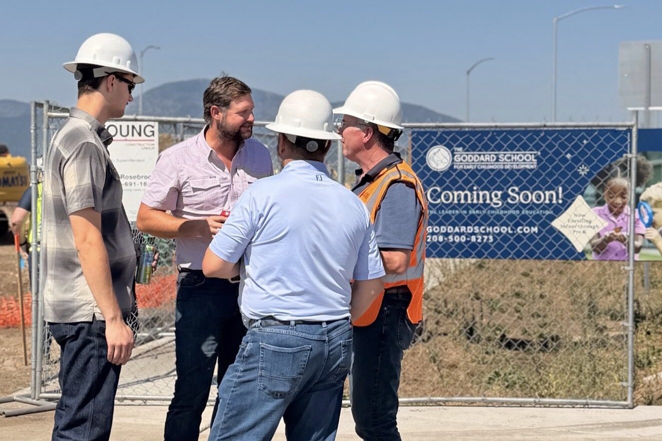 Four people in hard hats talking beside a fenced construction site